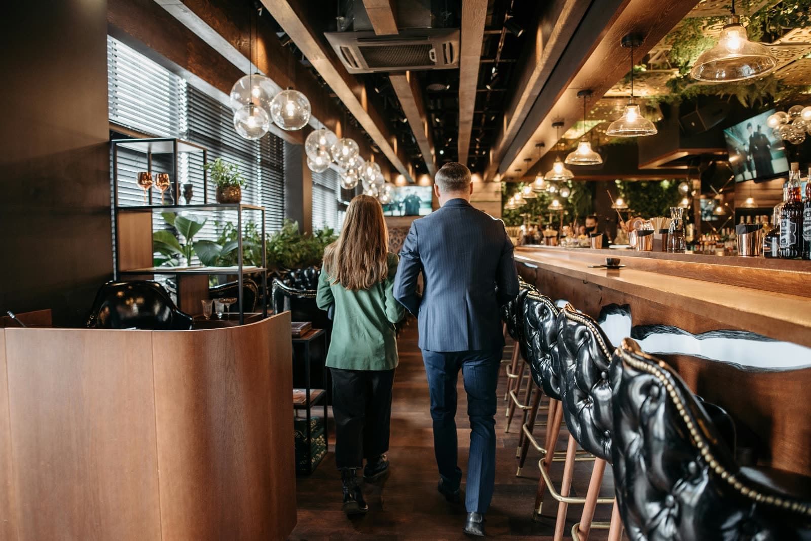 A couple walking into a wide, candlelit bar — arriving at the room